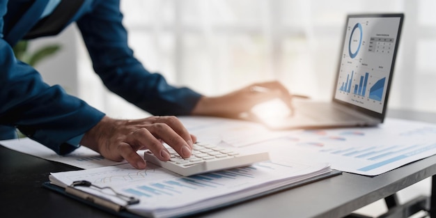 Close up Businessman using calculator and laptop for calculating finance tax accounting statistics and analytic research concept