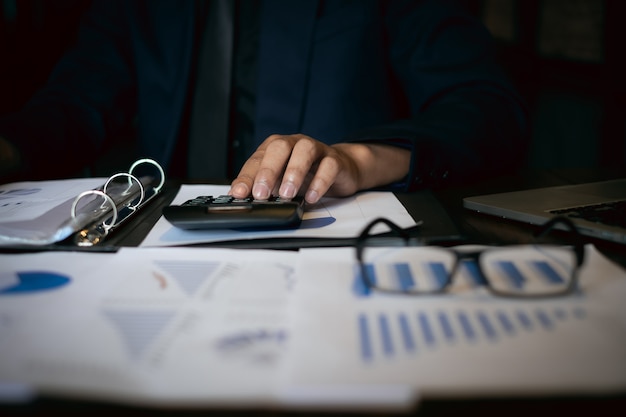 Foto chiuda sull'uomo d'affari facendo uso del calcolatore e del computer portatile per fanno le finanze di per la matematica sullo scrittorio di legno