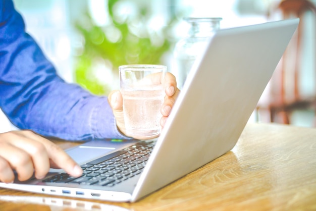 Photo close-up of businessman using laptop while drinking water on table