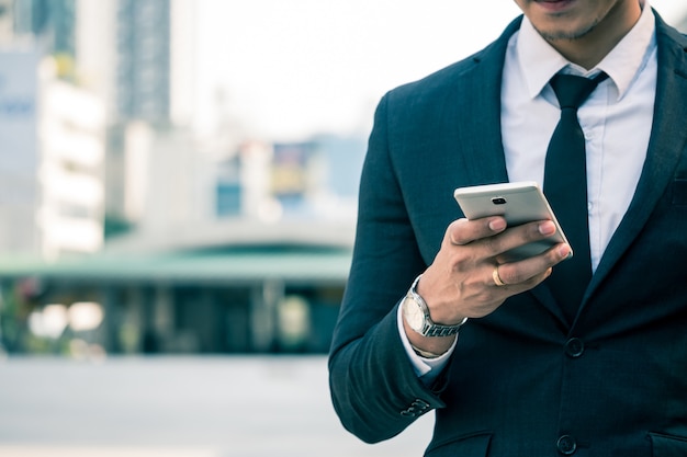 Close up of businessman using smart phone with urban scene background.