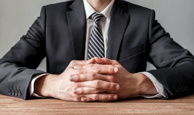 Close up of a businessman at a wooden table with crossed hands