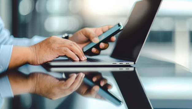 Близкий взгляд на руки бизнесмена, использующего смартфон над клавиатурой ноутбука в современной офисной среде с синим освещением