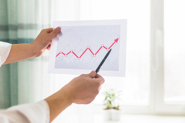 Close-up of a businessperson's hand analyzing graph at workplace