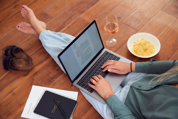 Close up of businesswoman at end of day with wine in loungewear and suit on laptop working at home