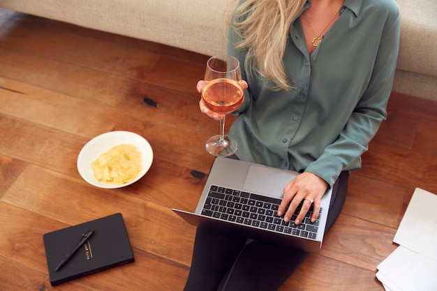 Крупный план деловой женщины в конце дня с вином в домашней одежде и костюме на ноутбуке, работающем дома