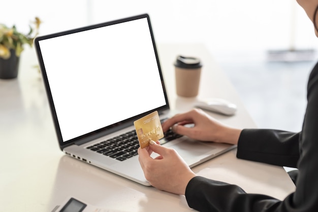 Close up. Businesswoman hand holding credit card shopping online by using a laptop blank white screen at the office.