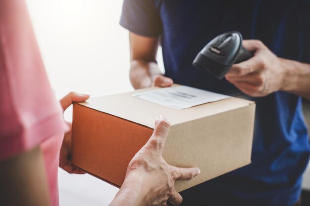 Photo close-up of businesswoman holding box while man scanning box with barcode scanner