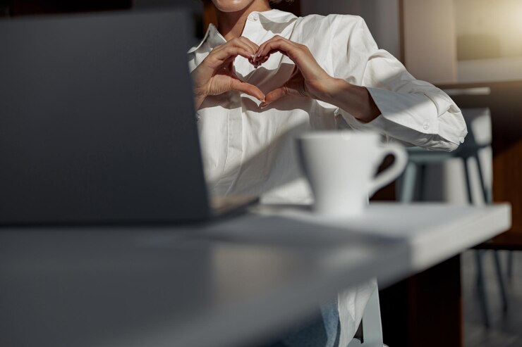 Close up of businesswoman making video call to friends and showing sign love sitting in office