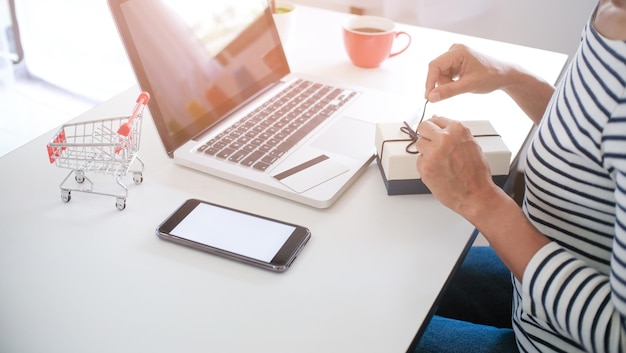 Close-up of businesswoman opening gift with laptop on table