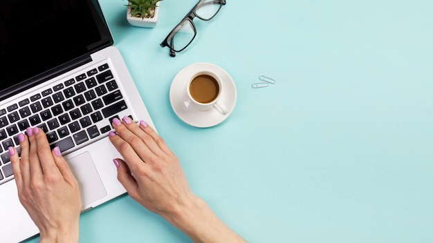 Primo piano della mano della donna di affari che scrive sul computer portatile con la tazza di caffè, occhiali e