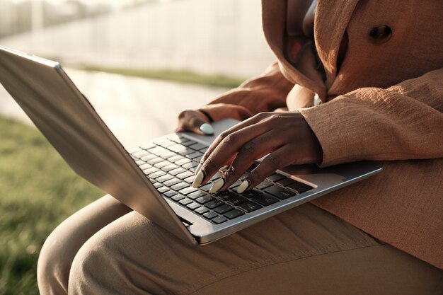 Close-up of businesswoman sitting outdoors with laptop on her knees and working online