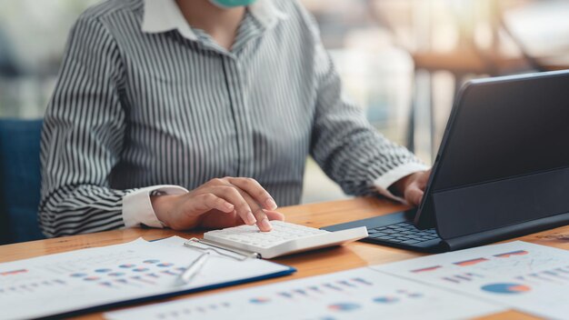 Close up of a businesswoman with hand using a calculator to calculate business principles. Accounting statistics concept at the office.