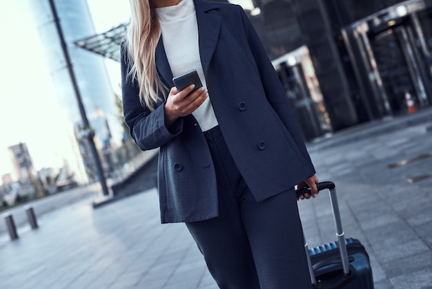 Foto primo piano di una donna d'affari con telefono e valigia che cammina