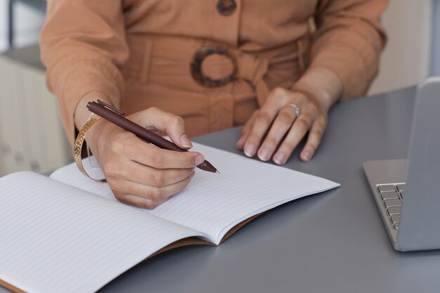 Primo piano della donna di affari che scrive i piani aziendali nel blocco note lavorando sul suo posto di lavoro