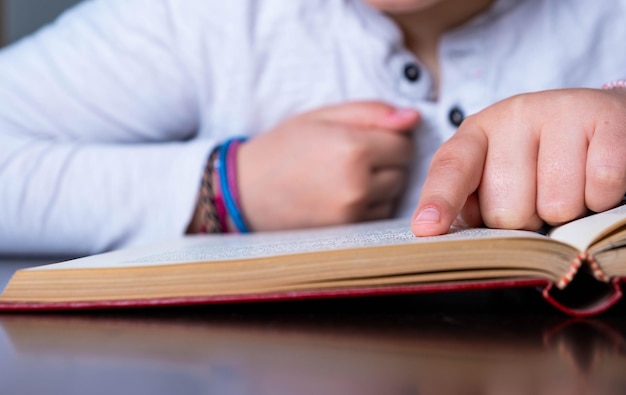 Close-up by the hand of a girl pointing with her finger her advance in reading. World Book Day, Chil