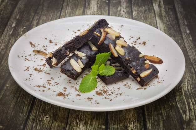 Close up of cake chocolate brownies with nuts and mint on white plate