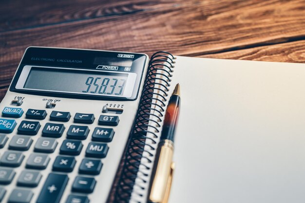 Photo close up of calculator pen and notebook on a wooden background concept of business finance education