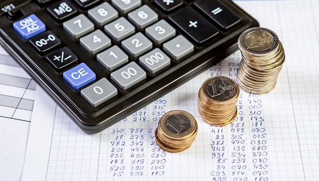 Close up of a calculator and three stack coins on a business background.
