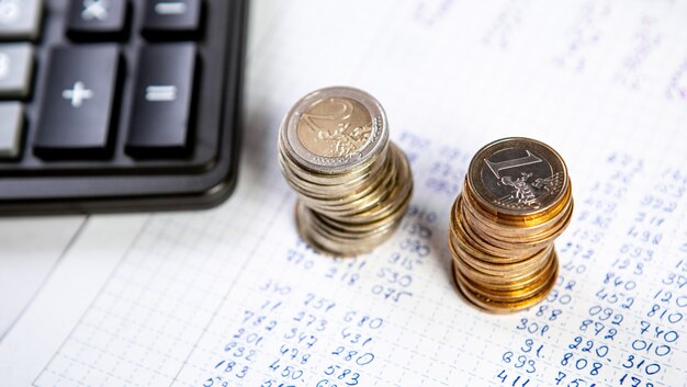 Close up of a calculator and two stacks coins on a business background.