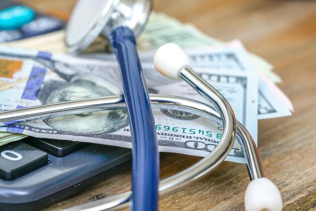 Photo close-up of calculator with stethoscope and paper currencies on table