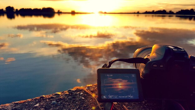 Photo close-up of camera on sea against sky during sunset