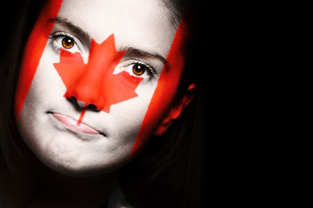 暗い背景の上の女性の顔のカナダの旗のクローズアップ