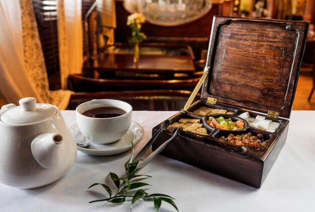 Photo close-up of candied fruit in wooden box by teapot and cup on table at restaurant