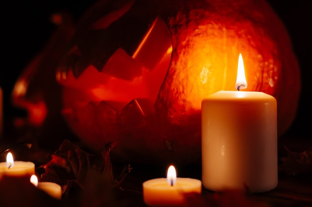 Close-up of a candle with fire on the background of a pumpkin with a carved face for the celebration of death. Halloween concept.