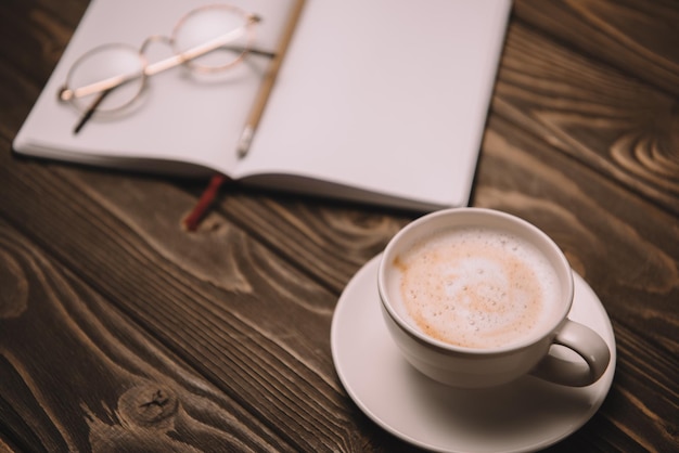 Close up of cappuccino notebook and eyeglasses on wooden table