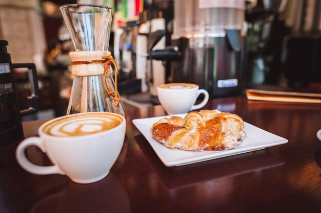 Photo close-up of cappuccinos and croissant served on table
