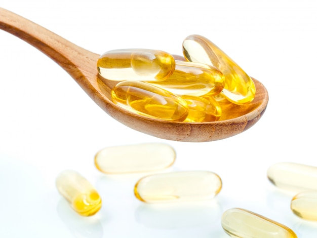 Close up capsules fish oil in wooden spoon .