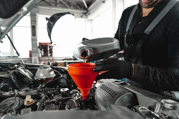 Chiuda in su del lavoratore di servizio auto versando olio nuovo nel motore dell'auto