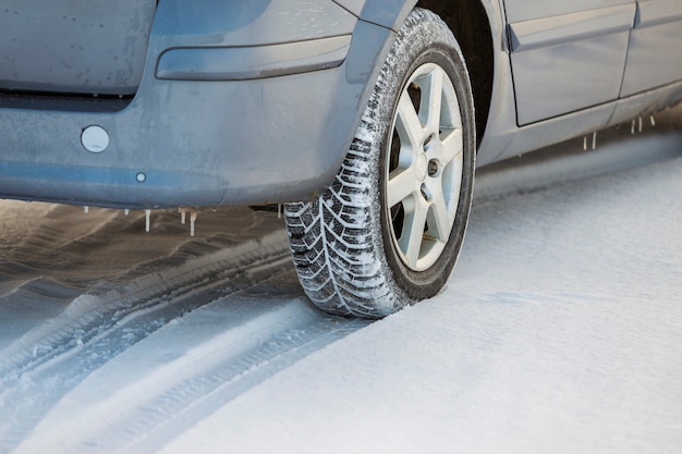 Close up of a car tire parked on snowy road on winter day. Transportation and safety concept.