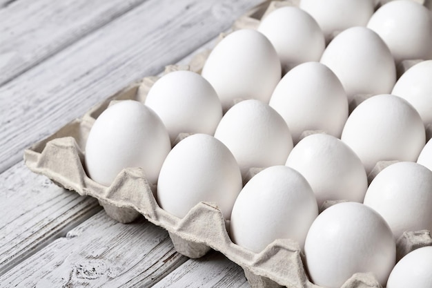 Primo piano del vassoio di cartone con uova di gallina bianche su fondo di legno