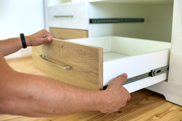 Close up of carpenter hands installing wooden drawer on sliding skids in contemporary cupboard cabinet.