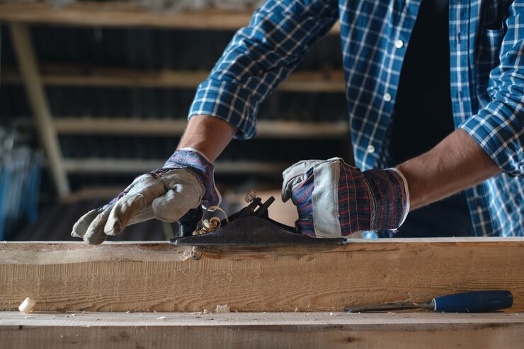 Close-up of the carpenter's hands in gloves with a planer machine handle wood, manual labor, safety, rules of work with the tool