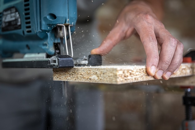 Close-up of a carpenter's hands in the process of cutting wood with a jigsaw.