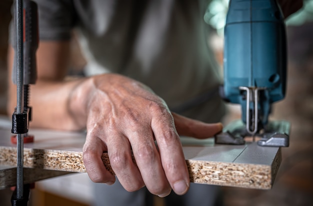 Close-up of a carpenter's hands in the process of cutting wood with a jigsaw.