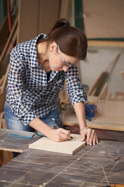 Close up carpenter woman in glasses with tape measure and blackboard in workshop