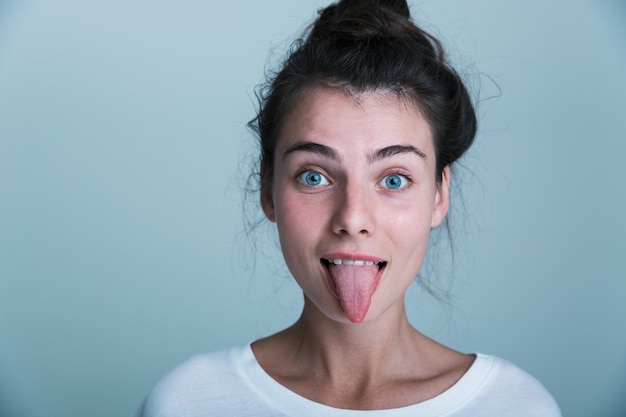 Photo close up of a casual beautiful young girl isolated over blue background, sticking her tongue out