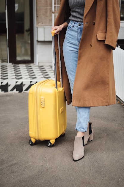 Close up casual girl in coat standing with yellow suitcase outdoor