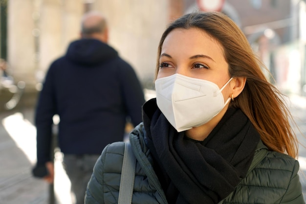 Primo piano di una donna casual che cammina per una strada cittadina indossando una maschera protettiva kn95 ffp2 che guarda di lato