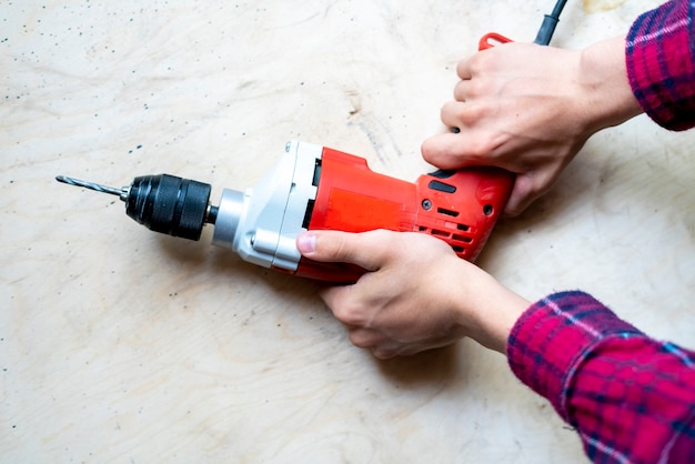 Close up casual worker holding electric drill and repair furniture at home f