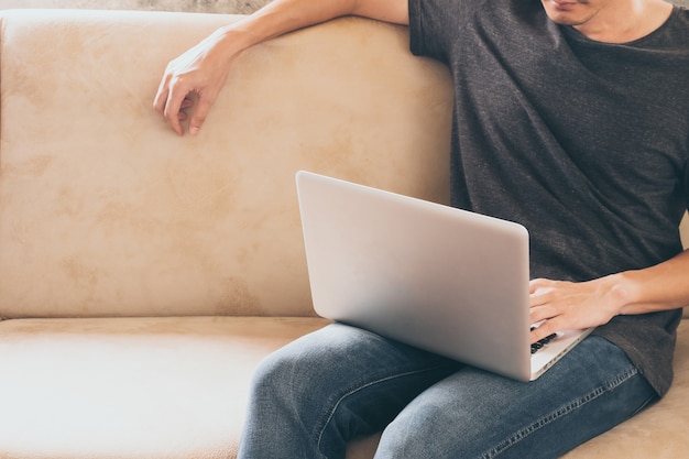 Close up of casual young man sitting on sofa and using a laptop at home.