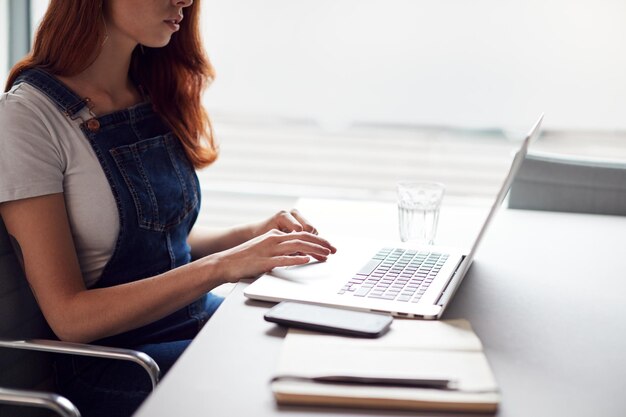 Photo close up of casually dressed young businesswoman working on laptop at desk in modern workplace