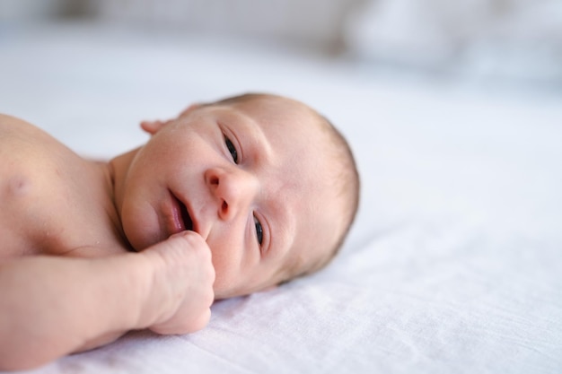 Close up of caucasian hairy brunet cute newborn baby lying on back on white sheet looking at cameraNaked one week old child half body shot copy space for text