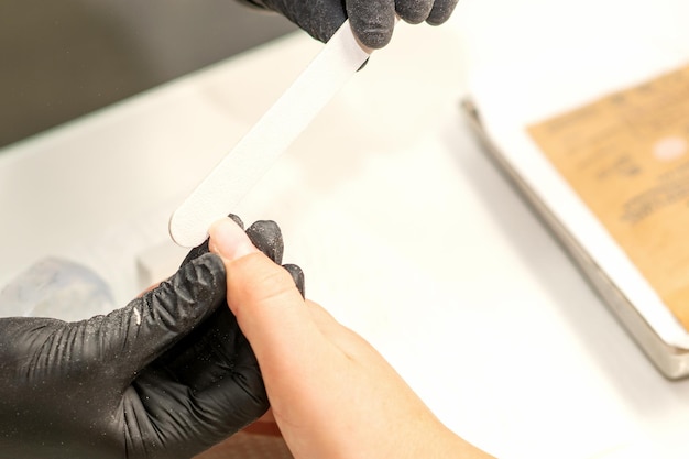 Close up of the caucasian hands of a professional manicurist are filing the nails of a young woman Young caucasian woman receiving a manicure by a beautician with a nail file in a nail salon