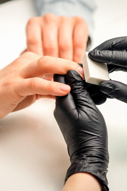 Close up of the caucasian hands of a professional manicurist are filing the nails of a young woman Young caucasian woman receiving a manicure by a beautician with a nail file in a nail salon