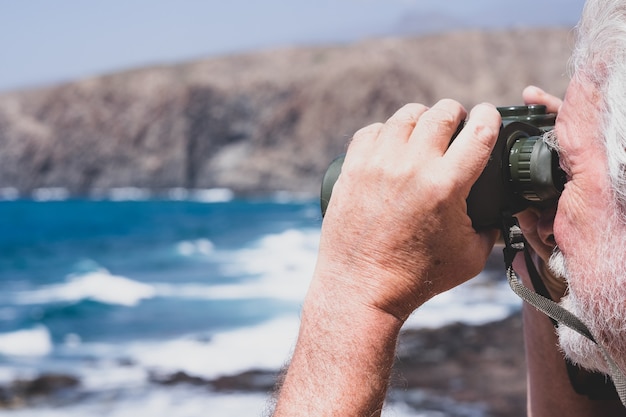 Close-up of caucasian man hand holding binoculars looking at sea, mountain. Senior retired enjoying freedom and knowledge