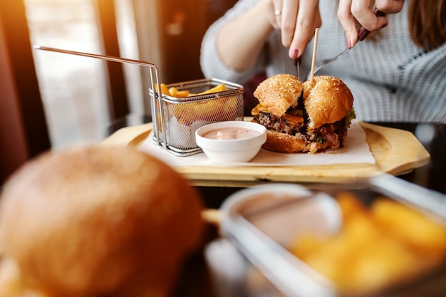 Close up of Caucasian woman eating delicious burger while sitting in the restaurant.